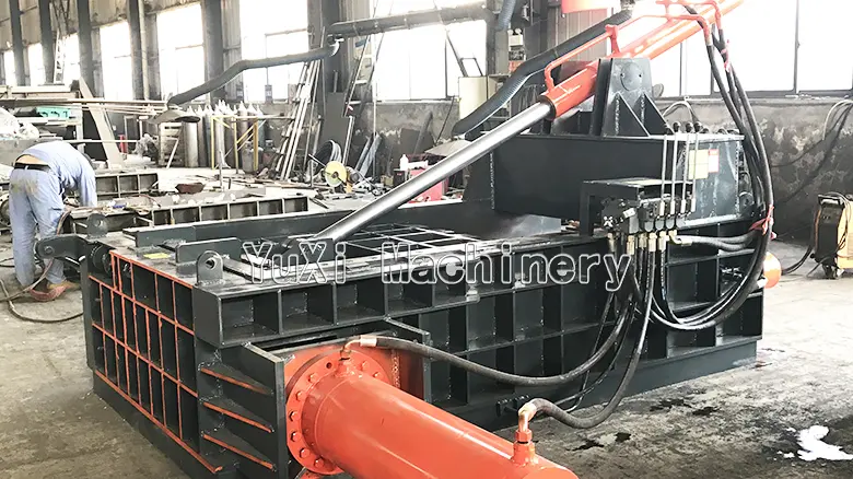 Industrial scrap metal baler working in a factory setting, with operator nearby